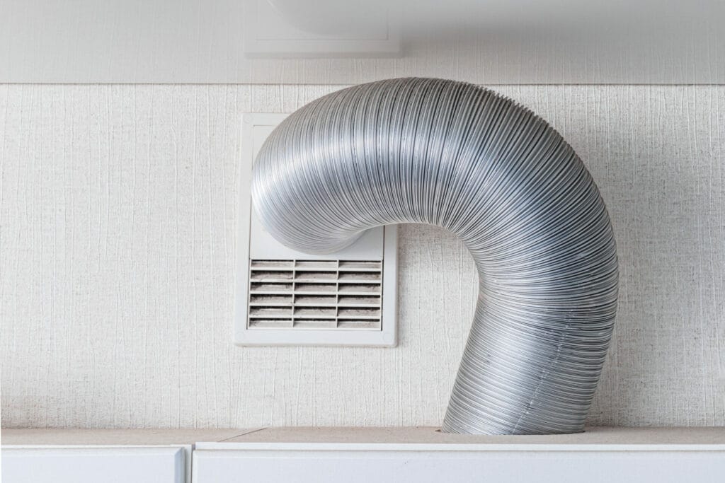 A flexible silver air duct, essential for dryer vent cleaning, is connected to a white wall vent, curving downward onto a white countertop.